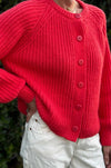 Close-up of bright red cardigan sweater with buttons and oversized sleeves worn with white pants