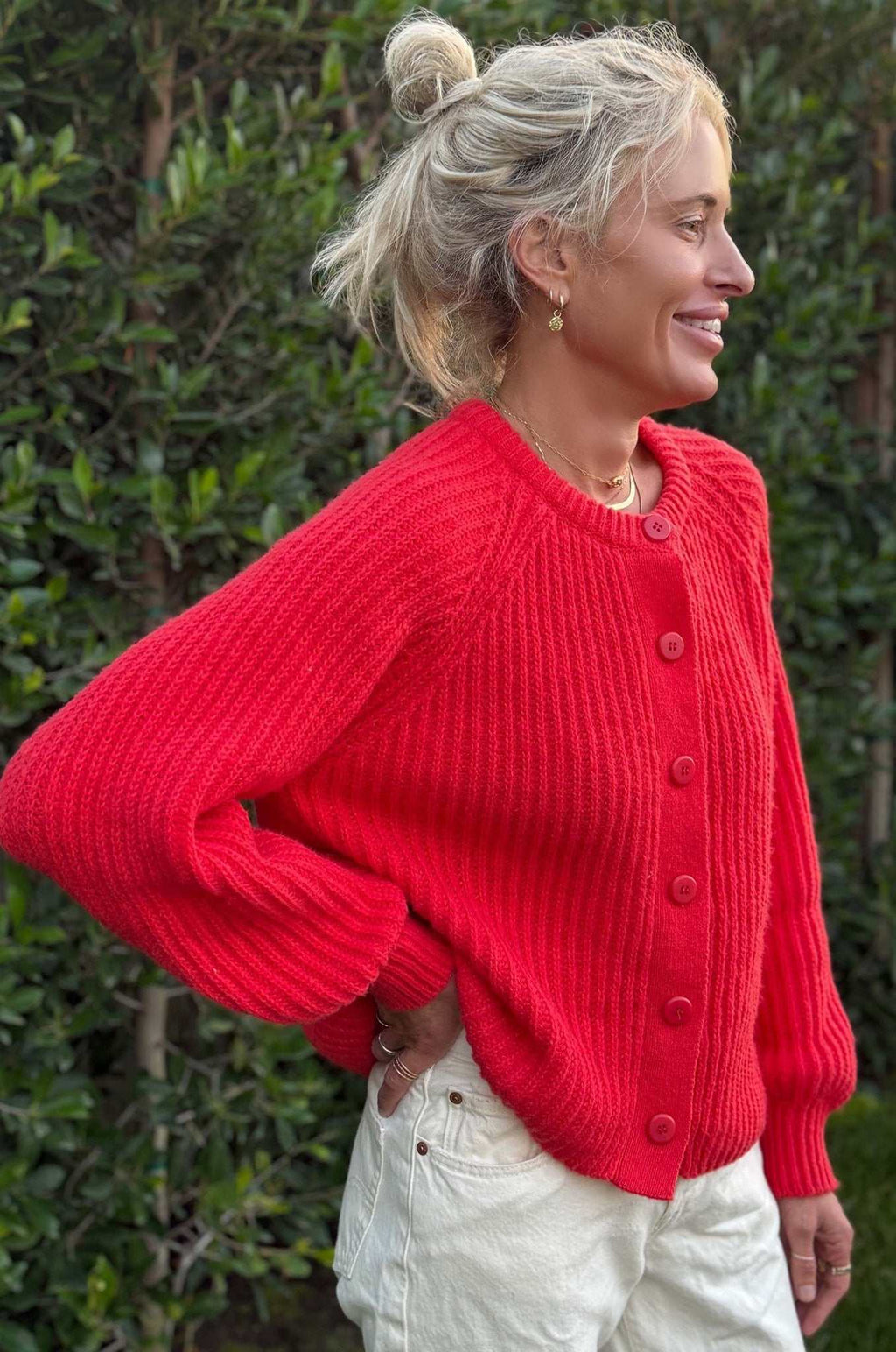 Close-up of bright red cardigan sweater with buttons and oversized sleeves worn with white pants