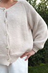 tan cardigan button down sweater with oversized sleeves and knit texture worn with white pants outdoors