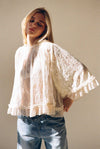 Woman wearing ivory lace top with high neck, ruffle trim, and flowy sleeves paired with jeans