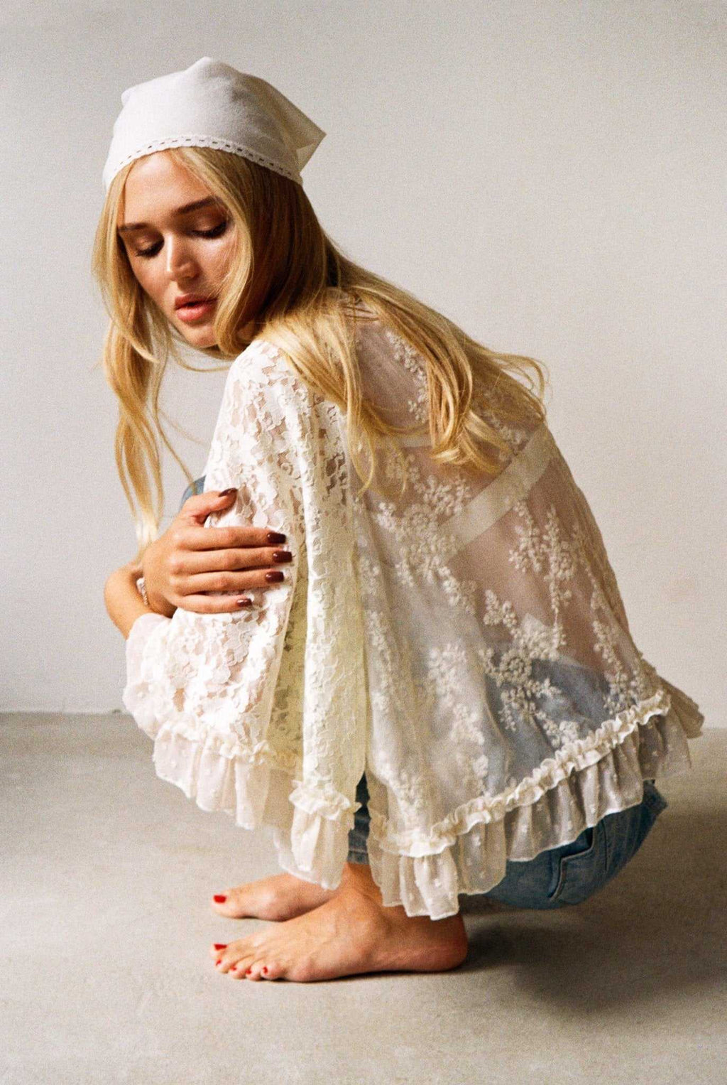 Woman wearing ivory lace top with ruffle trim and flowy sleeves sitting barefoot