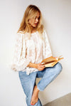 Woman wearing ivory lace top with circular lace design and ruffle details reading a book